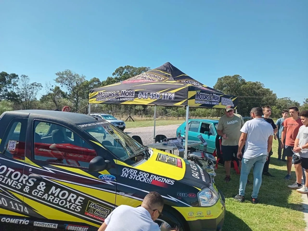 Motors & More Gqeberha branded tent at an outdoor event with car and engine samples